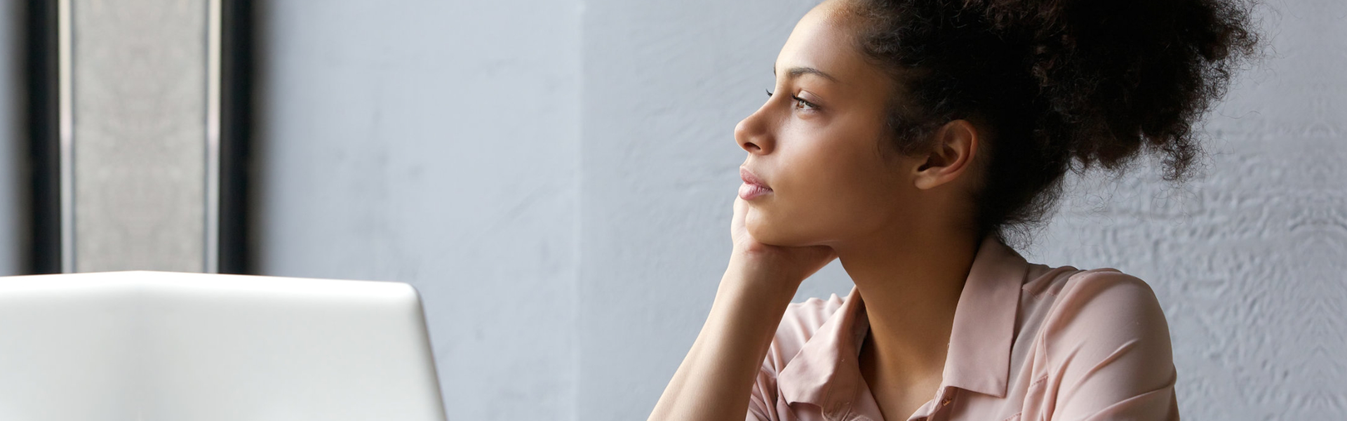 young african american woman looking out window when working on laptop