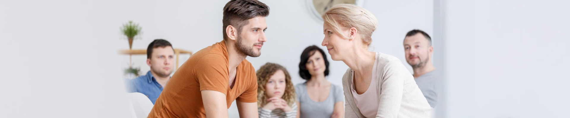 Young man and middle-aged woman sitting and looking into each other's eyes with other people in the background